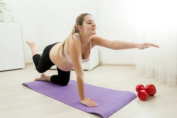 Joven madre embarazada haciendo ejercicio y estiramiento en la esterilla de fitness — Foto de Stock