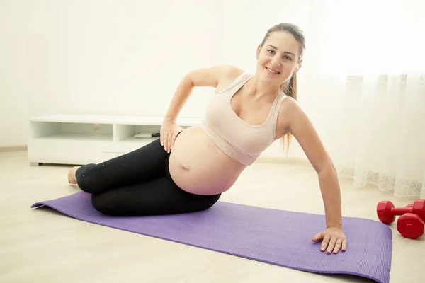 Sorridente donna incinta che esercita sul tappeto fitness a casa — Foto Stock