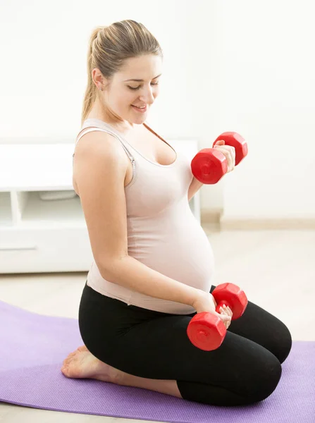 Donna incinta seduta sul tappeto fitness e che esercita con il peso — Foto Stock