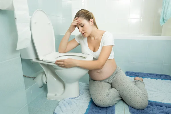 Беременная женщина опирается на унитаз и чувствует себя больной — стоковое фото