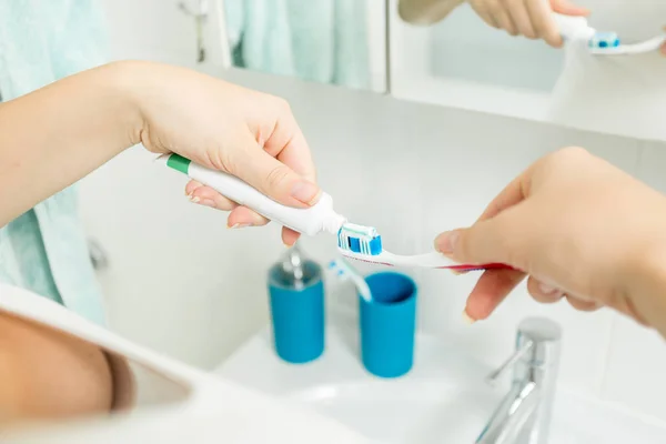 Imagen de primer plano de la mujer poniendo pasta de dientes en el cepillo de dientes en la taza de un —  Fotos de Stock