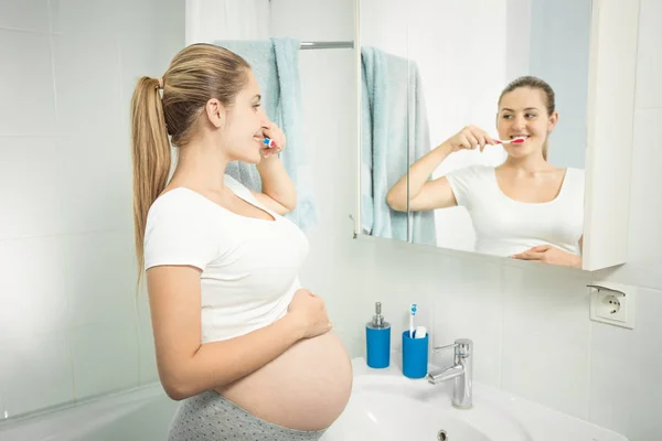 Retrato de una hermosa mujer joven cepillándose los dientes en el espejo en ba —  Fotos de Stock