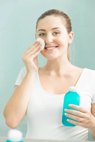 Mujer morena sonriente mirando en el reflejo y usando lotio — Foto de Stock