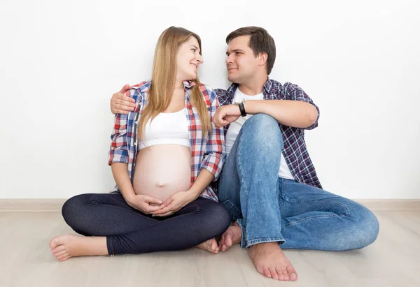 Zwanger koppel in jeans en shirts zittend op de vloer tijdens lege ro — Stockfoto