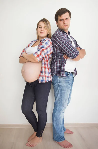 Joven pareja embarazada apoyada en la pared blanca en la habitación vacía — Foto de Stock