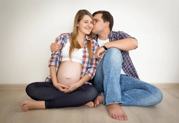 Toned portrait of happy pregnant couple sitting on floor and kis — Stock Photo, Image