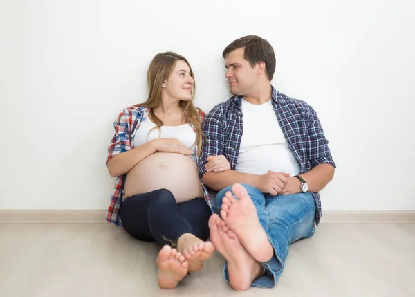 Smiling barefoot pregnant couple posing on floor at empty room — Stock Photo, Image