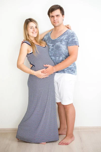 Lyckligt leende gravida par i randiga kläder poserar mot — Stockfoto