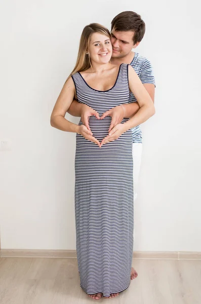 Happy hugging pregnant couple holding hands in shape of heart — Stock Photo, Image