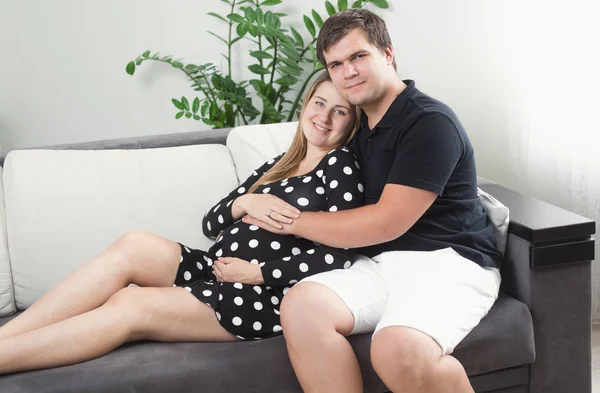 Portrait of happy pregnant woman and man relaxing on sofa at liv — Stock Photo, Image