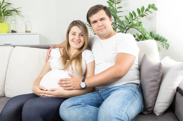 Feliz jovem casal esperando para o bebê sentado no sofá na vida ro — Fotografia de Stock