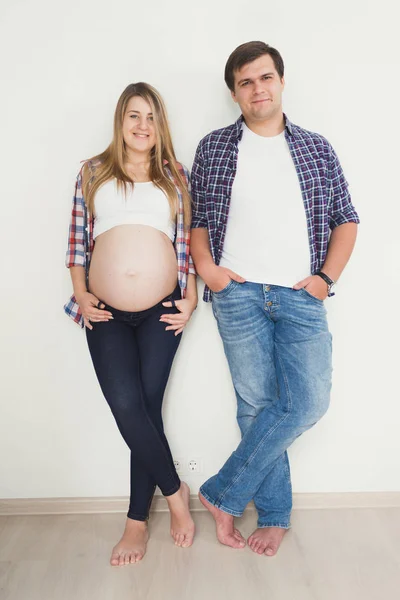 Mutlu gülümseyen çift kot pantolon ve gömlek poz bebek bekliyor — Stok fotoğraf