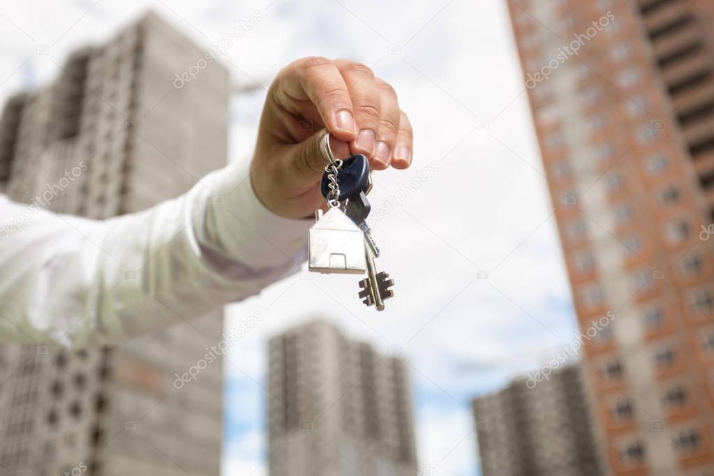 Male hand holding keys from new home on background of buildings 