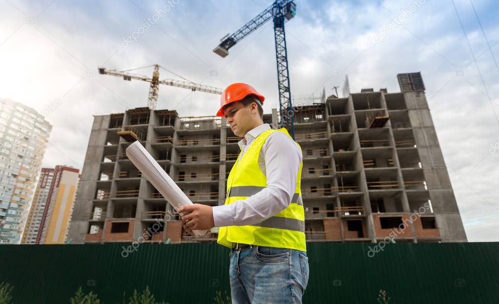 Young construction engineer in hardhat on building site with wor