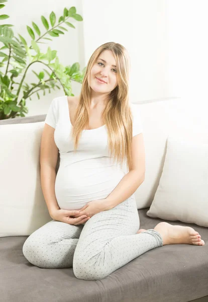Linda mãe grávida sorridente sentada no sofá na sala de estar — Fotografia de Stock