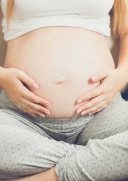 Jovem grávida sentada no sofá e de mãos dadas na barriga — Fotografia de Stock