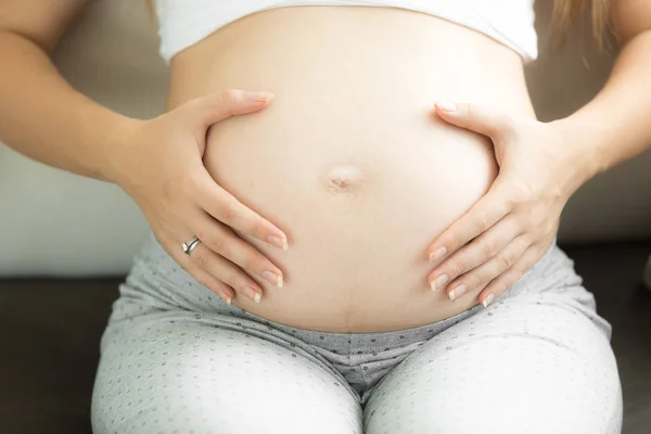 Крупный план молодой беременной женщины, держащейся за руки на животе — стоковое фото