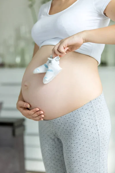 Unga gravid kvinna poserar med baby tossor på magen på living — Stockfoto