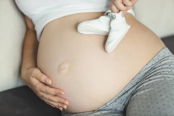 Primer plano de la mujer embarazada sosteniendo calcetines de bebé en el vientre — Foto de Stock