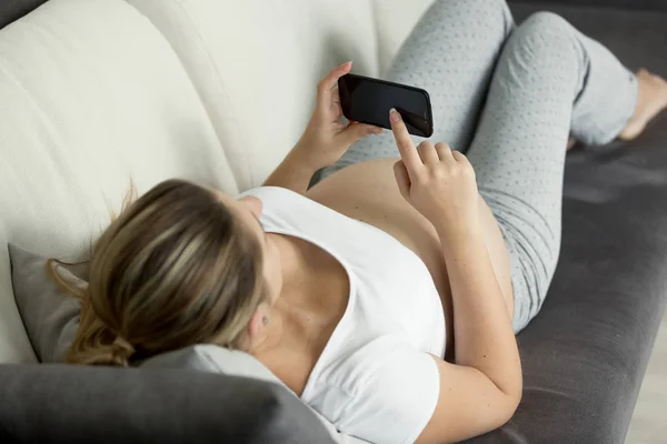 Young pregnant woman lying on sofa and looking at ultrasound emb — Stock Photo, Image