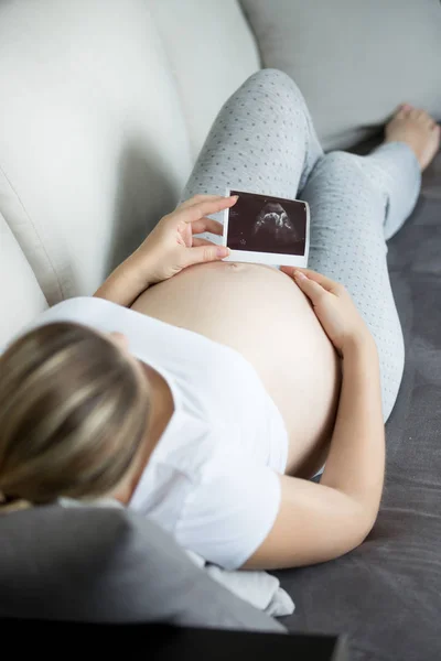 Fotografie de aproape a unei tinere gravide care se relaxează pe canapea și arată — Fotografie, imagine de stoc