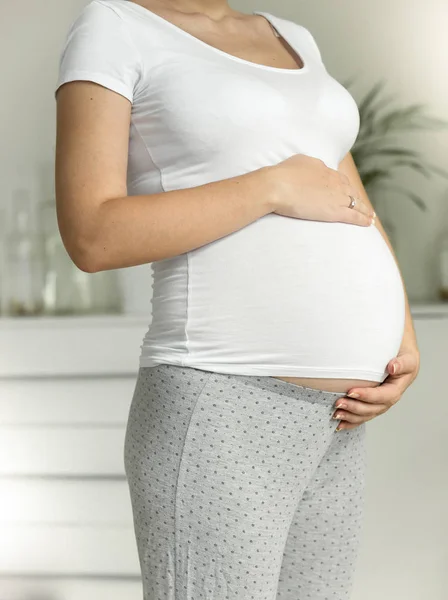 Fiatal terhes nő tartja kezében a hasa pizsamában — Stock Fotó