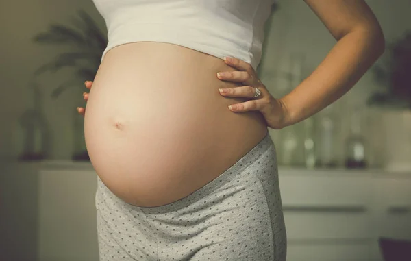 Imagem tonificada da mulher grávida posando na janela e de mãos dadas — Fotografia de Stock