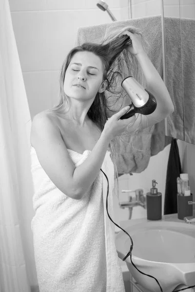 Black and white image of young woman in with hairdryer at bathro