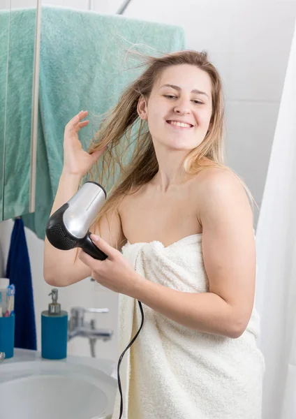 Молодая женщина в полотенце сушит волосы в ванной комнате — стоковое фото