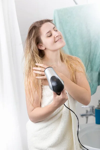 Hermosa mujer cubierta de toalla de baño con secador de pelo en el baño — Foto de Stock
