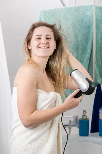 Portret van lachende jonge vrouw drogen lange haren in de badkamer — Stockfoto