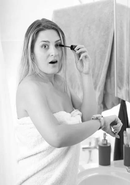 Black and white portrait of woman applying mascara at bathroom a