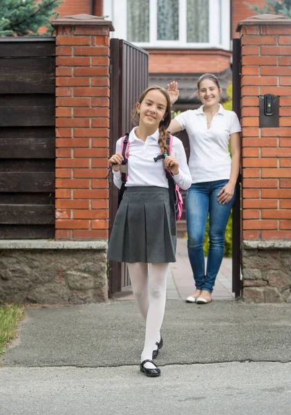 Smiling girl going out the house to school. Mother standing in d