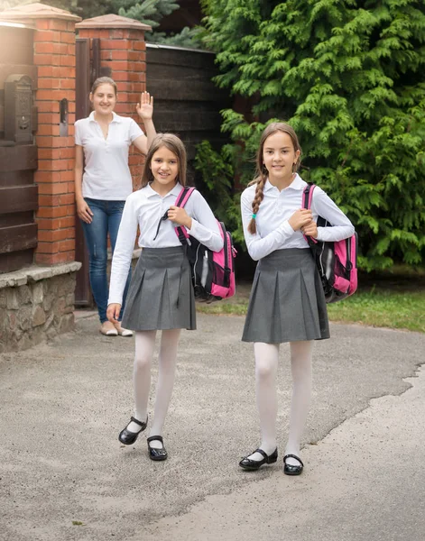 Dos chicas sonrientes lindas con bolsas que salen de casa para la escuela por la mañana —  Fotos de Stock