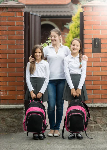 Улыбающаяся мать, стоящая в дверях с двумя дочерьми, уходящими из дома — стоковое фото