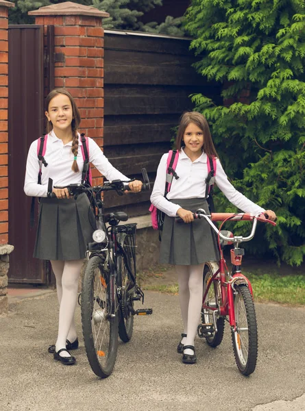 Тонированное изображение милых улыбающихся девочек, идущих в школу на велосипедах — стоковое фото