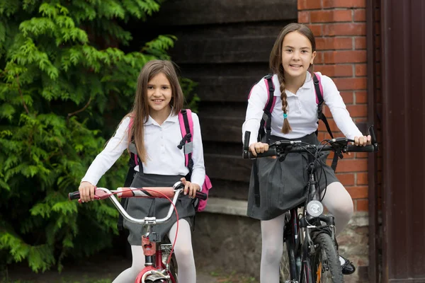 Deux filles souriantes heureuses en uniforme se rendant à l'école à vélo — Photo