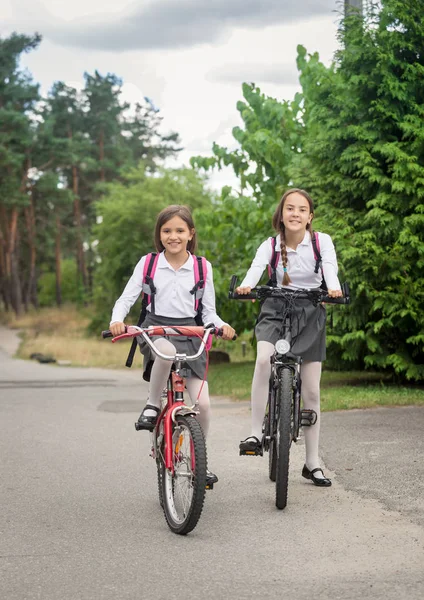 İki gülümseyen kız okula bisiklet sürme — Stok fotoğraf