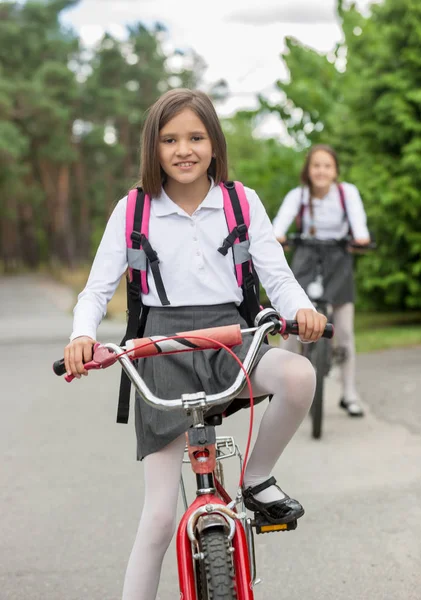 Deux filles heureuses en uniforme scolaire à vélo le matin — Photo