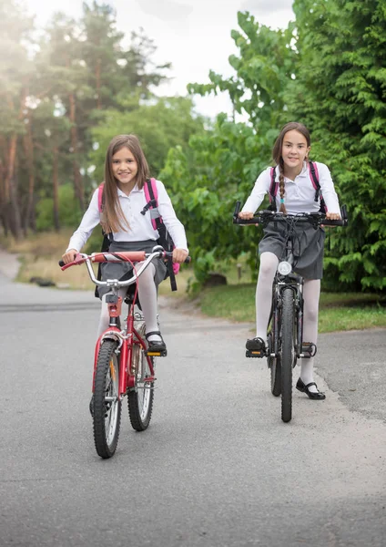 Dos hermosas colegialas sonrientes cabalgando a la escuela en bicicletas — Foto de Stock
