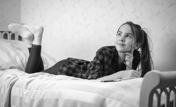 Black and white image of thoughtful teenage girl lying on bed at — Stock Photo, Image