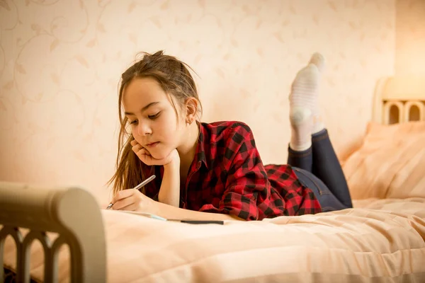 Красивая улыбающаяся девочка лежит на кровати и пишет в дневнике — стоковое фото