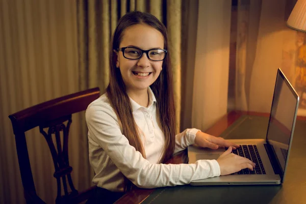 Retrato de colegial sorrindo usando laptop no quarto escuro — Fotografia de Stock