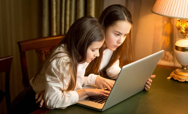 Deux écolières faisant leurs devoirs à l'ordinateur portable la nuit — Photo