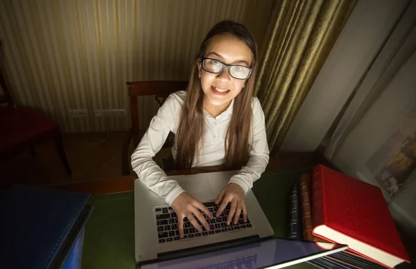 Smiling schoolgirl in white shirt doing homework at laptop in da — Stock Photo, Image