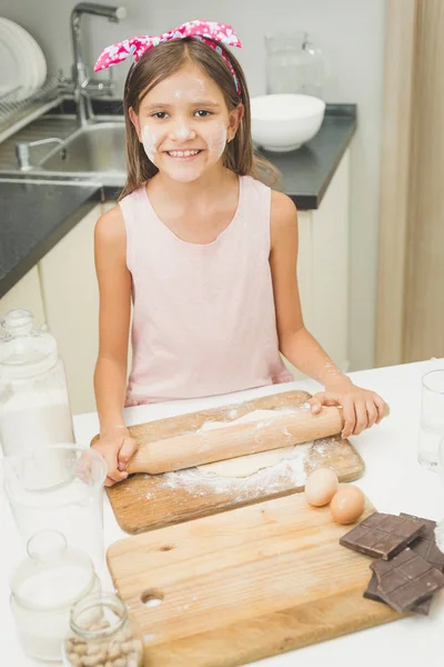 Ritratto di ragazza sorridente rotolamento pasta con spillo di legno su kitche — Foto Stock