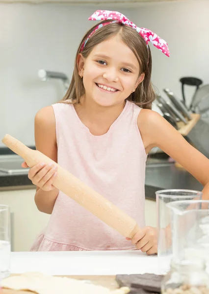 Porträt des niedlichen lächelnden Mädchens mit hölzernem Nudelholz, während m — Stockfoto