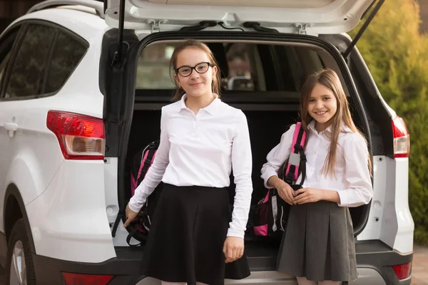 Portret van twee lachende meisjes nemen schooltassen uit auto trun — Stockfoto