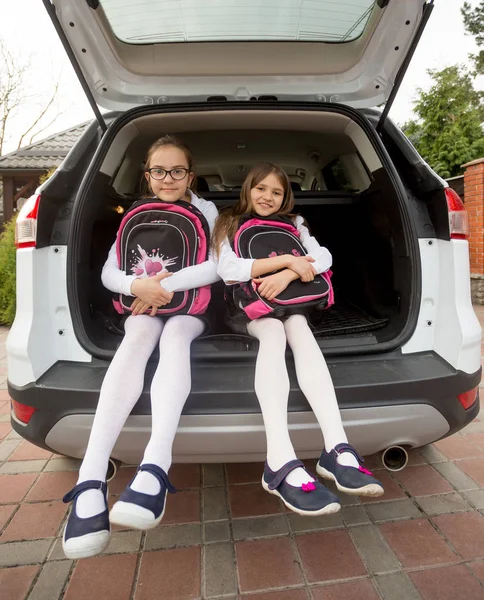 Twee schattige schoolmeisjes poseren in open auto kofferbak met zakken — Stockfoto