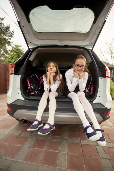 Twee leuke meisjes in school uniform zitten open auto kofferbak — Stockfoto